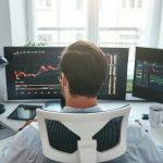Trading stocks online. Back view of young businessman or trader working with graph and charts on